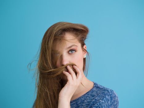 Portrait of a beautiful positive young woman while playing with her long silky hair isolated on blue background