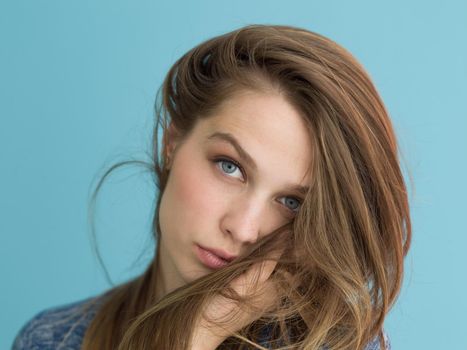 Portrait of a beautiful positive young woman while playing with her long silky hair isolated on blue background