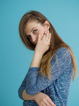 Portrait of a beautiful positive young woman while playing with her long silky hair isolated on blue background