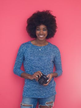 portrait of a smiling pretty african american girl taking photo on a retro camera isolated over pink background