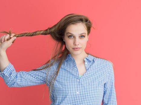 Portrait of a beautiful positive young woman while playing with her long silky hair isolated on red background