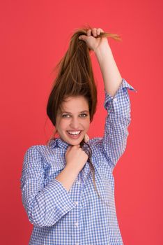 Portrait of a beautiful positive young woman while playing with her long silky hair isolated on red background