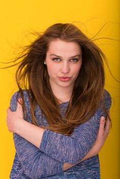 Portrait of a beautiful positive young woman while playing with her long silky hair isolated on yellow background