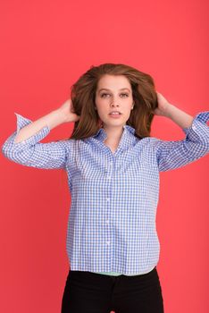 Portrait of a beautiful positive young woman while playing with her long silky hair isolated on red background