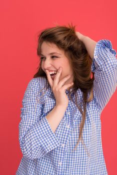 Portrait of a beautiful positive young woman while playing with her long silky hair isolated on red background