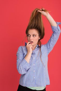 Portrait of a beautiful positive young woman while playing with her long silky hair isolated on red background