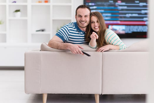 Young couple on the sofa watching television together in their luxury home