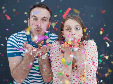 handsome young couple celebrating new year and chrismas party while blowing confetti decorations to camera isolated over gray background