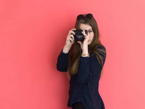 portrait of a smiling pretty girl taking photo on a retro camera isolated over red background