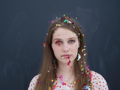 beautiful young woman celebrating new year and chrismas party while blowing confetti decorations to camera isolated over gray background