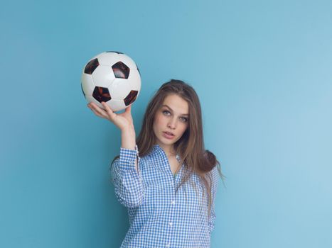 Portrait of a beautiful positive young woman while playing with a soccer ball isolated on blue background