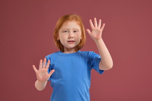 Portrait of cute redhead emotional little girl in blue t-shirt on red background. Beautiful studio portrait of female little caucasian person