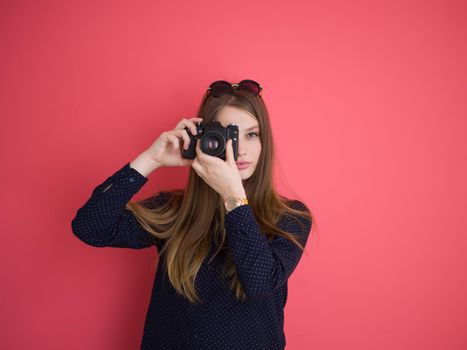 portrait of a smiling pretty girl taking photo on a retro camera isolated over red background