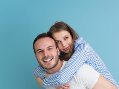 happy young man piggybacking his girlfriend isolated on blue background