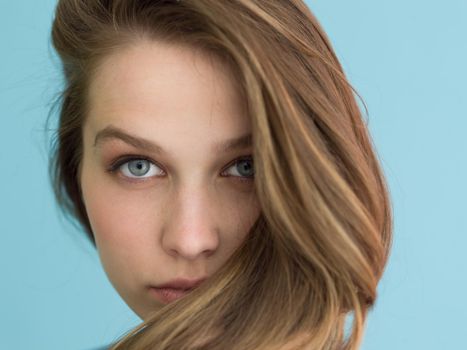 Portrait of a beautiful positive young woman while playing with her long silky hair isolated on blue background