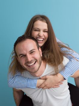 happy young man piggybacking his girlfriend isolated on blue background