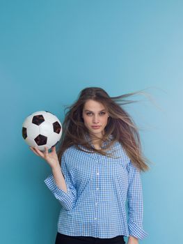 Portrait of a beautiful positive young woman while playing with a soccer ball isolated on blue background
