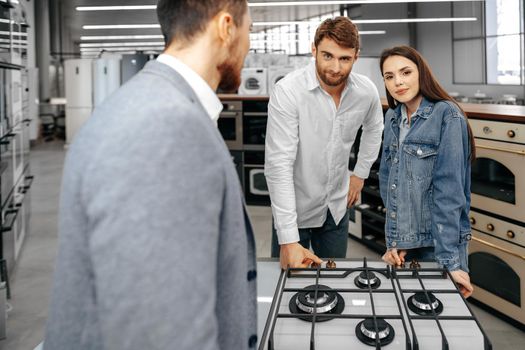 Male shop assistant helps young couple to choose new home appliance in hypermarket