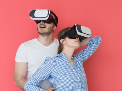 happy young couple getting experience using VR-headset glasses of virtual reality isolated over red background