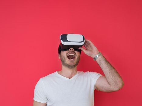 Happy man getting experience using VR headset glasses of virtual reality, isolated on red background