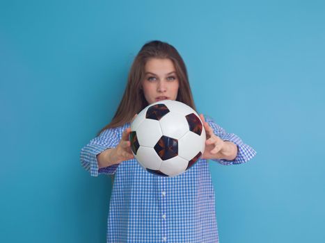 Portrait of a beautiful positive young woman while playing with a soccer ball isolated on blue background
