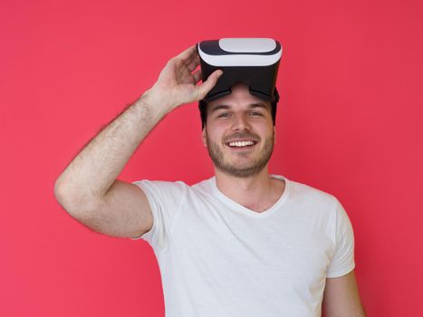 Happy man getting experience using VR headset glasses of virtual reality, isolated on red background