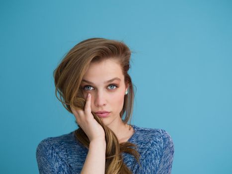 Portrait of a beautiful positive young woman while playing with her long silky hair isolated on blue background