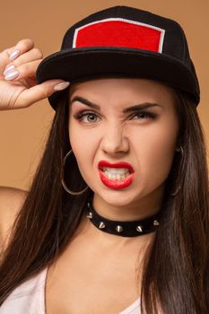 Hip-hop girl in cap with long dark hair. Fashion portrait of modern young woman in cap on beige background.