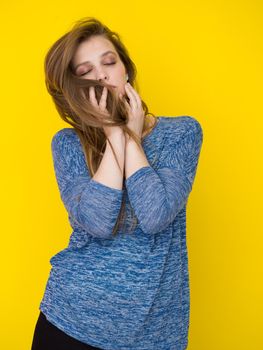 Portrait of a beautiful positive young woman while playing with her long silky hair isolated on yellow background