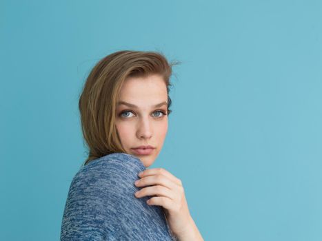 Portrait of a beautiful positive young woman while playing with her long silky hair isolated on blue background