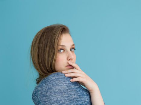 Portrait of a beautiful positive young woman while playing with her long silky hair isolated on blue background