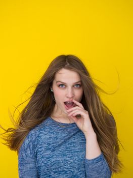Portrait of a beautiful positive young woman while playing with her long silky hair isolated on yellow background