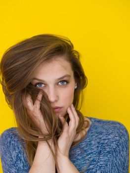 Portrait of a beautiful positive young woman while playing with her long silky hair isolated on yellow background