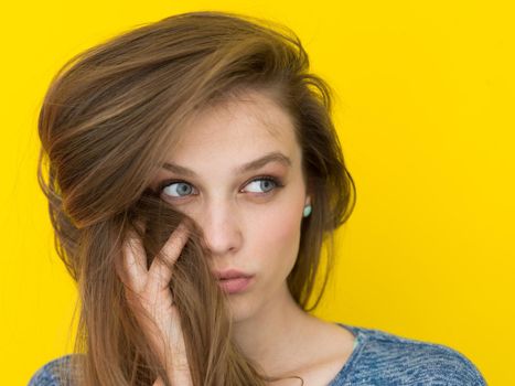 Portrait of a beautiful positive young woman while playing with her long silky hair isolated on yellow background