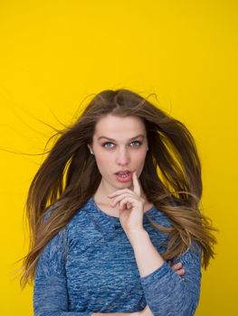 Portrait of a beautiful positive young woman while playing with her long silky hair isolated on yellow background