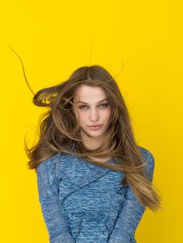 Portrait of a beautiful positive young woman while playing with her long silky hair isolated on yellow background