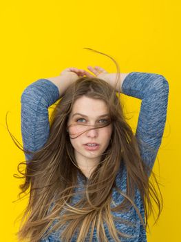Portrait of a beautiful positive young woman while playing with her long silky hair isolated on yellow background