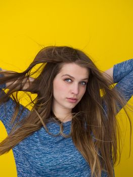 Portrait of a beautiful positive young woman while playing with her long silky hair isolated on yellow background