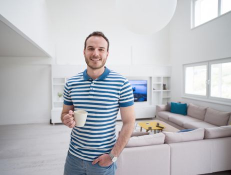 young handsome man drinking morning coffee by the window in his home