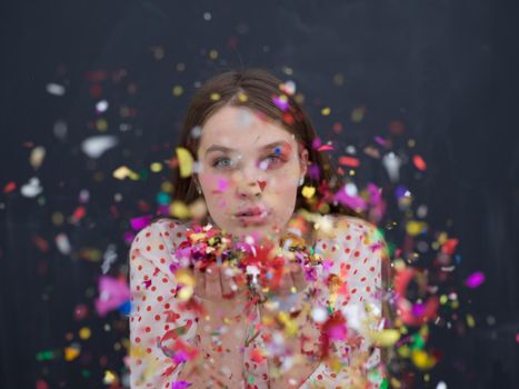 beautiful young woman celebrating new year and chrismas party while blowing confetti decorations to camera isolated over gray background