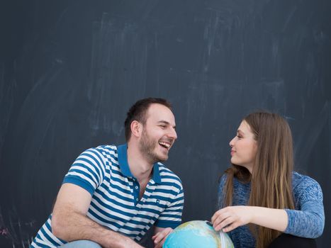 Young lovely couple in casual clothing investigating globe isolated over gray background