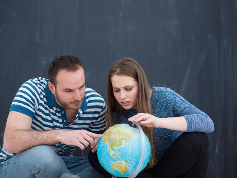 Young lovely couple in casual clothing investigating globe isolated over gray background