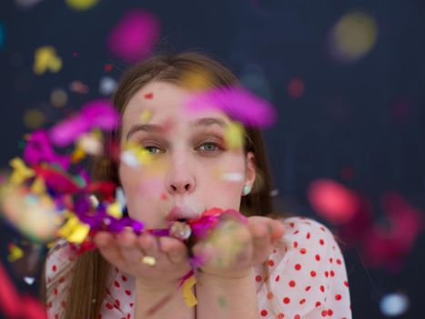 beautiful young woman celebrating new year and chrismas party while blowing confetti decorations to camera isolated over gray background