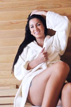 Pretty Young woman take a steam bath treatment at finish wooden sauna while wearing white towel