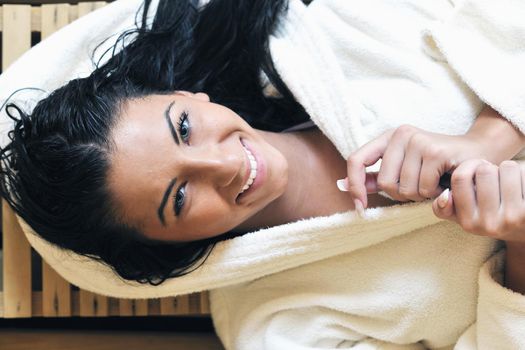 Pretty Young woman take a steam bath treatment at finish wooden sauna while wearing white towel
