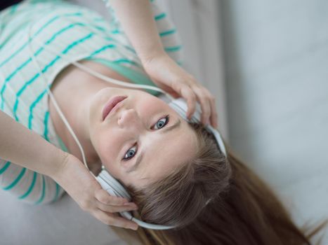 Young beautiful girl enjoying music through headphones, laying on sofa at home