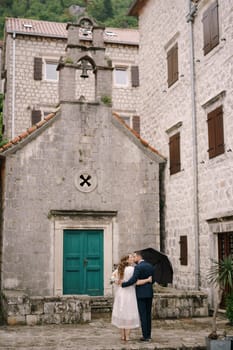 Groom embraces bride near the green door of the ancient church. Back view. High quality photo