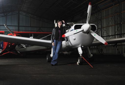 beautiful young woman model in fashion clothes posing in front of old private airplane 