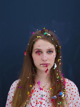 beautiful young woman celebrating new year and chrismas party while blowing confetti decorations to camera isolated over gray background