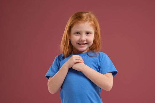 Portrait of cute redhead emotional little girl in blue t-shirt on red background. Beautiful studio portrait of female little caucasian person. She looks so happy